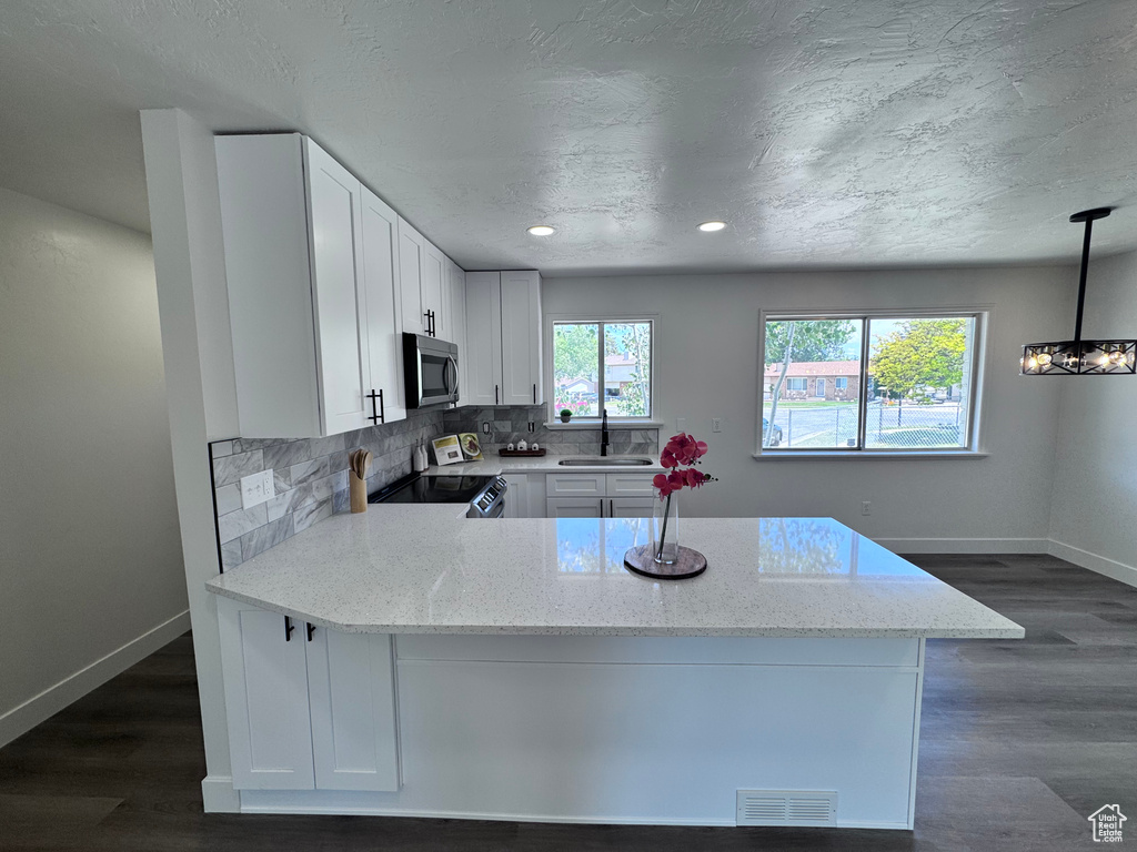 Kitchen with stainless steel microwave, electric range oven, a sink, baseboards, and light stone counters