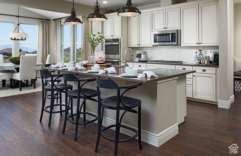 Kitchen with appliances with stainless steel finishes, dark countertops, decorative backsplash, a kitchen breakfast bar, and dark wood finished floors