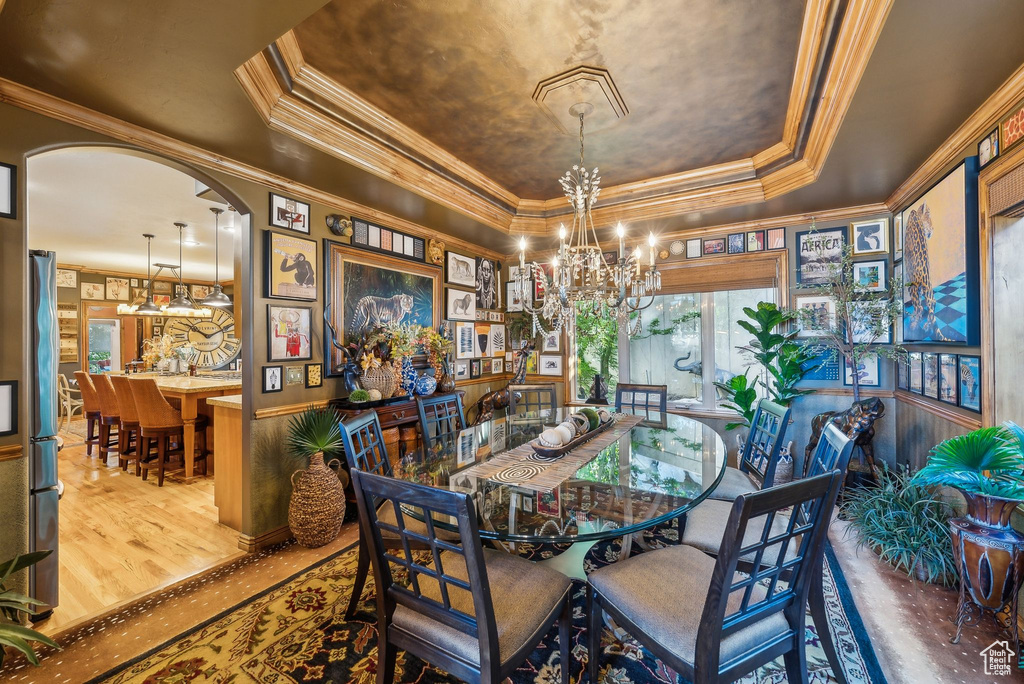 Dining area with a raised ceiling, a chandelier, ornamental molding, wood finished floors, and arched walkways