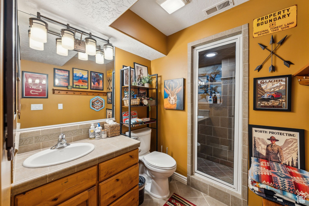 Bathroom with toilet, vanity, tile patterned flooring, a shower stall, and a textured ceiling
