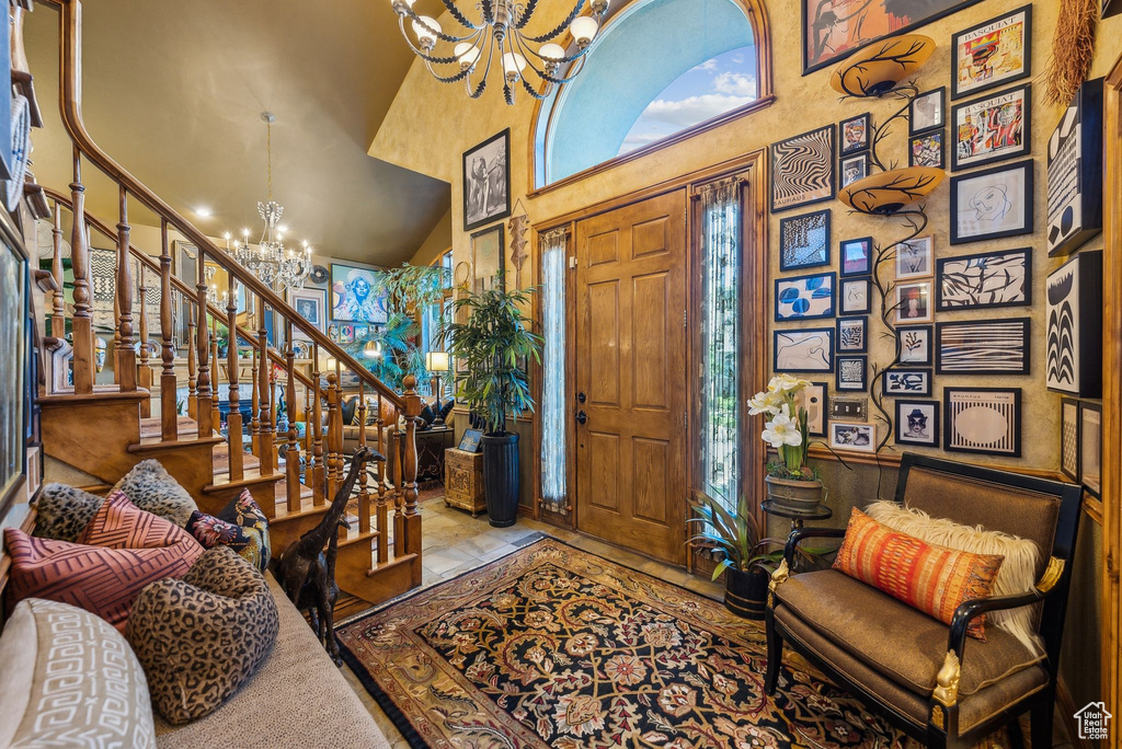 Foyer entrance featuring a chandelier, a towering ceiling, plenty of natural light, stone tile flooring, and stairs