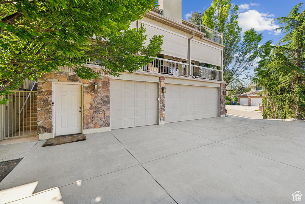 View of front of home featuring stone siding, concrete driveway, an attached garage, and a balcony
