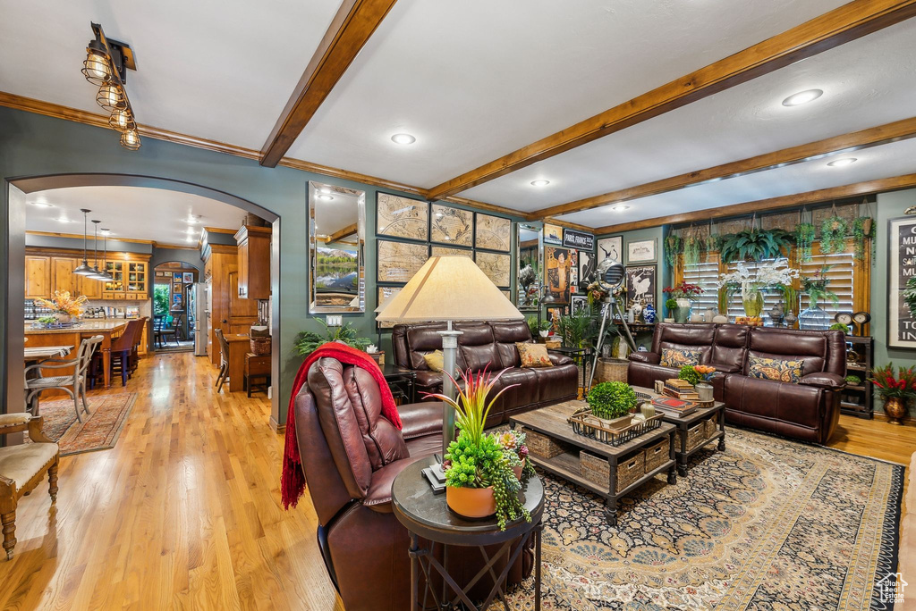 Living area with arched walkways, beam ceiling, ornamental molding, light wood-style flooring, and recessed lighting