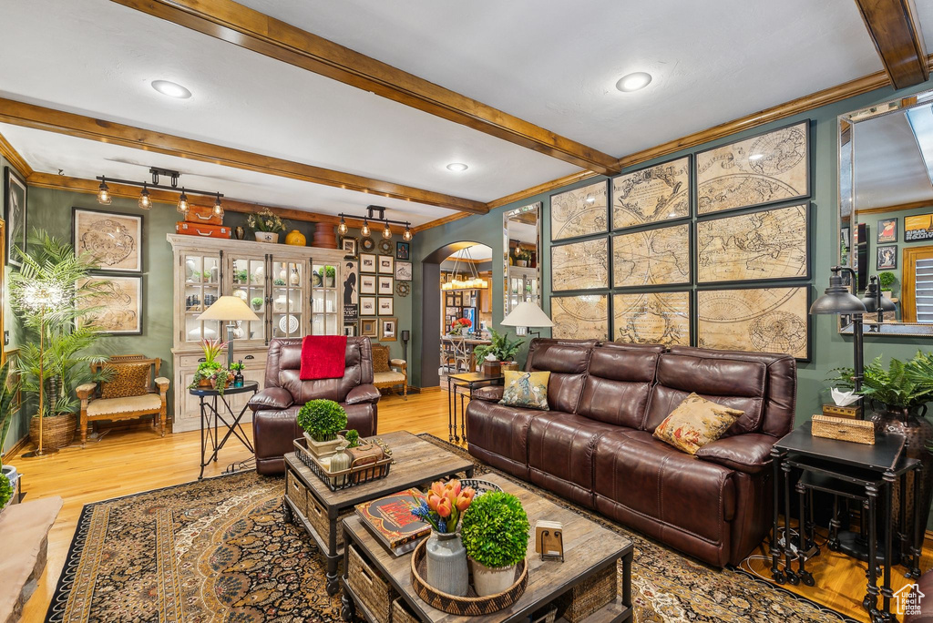 Living area with beam ceiling, arched walkways, wood finished floors, and crown molding
