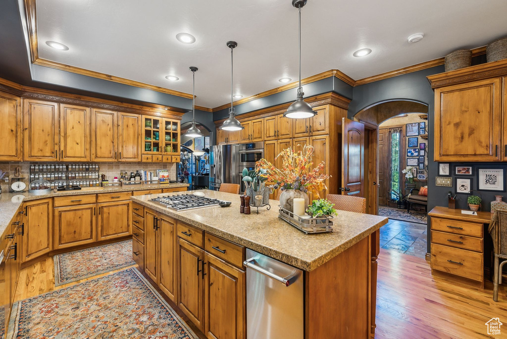 Kitchen featuring arched walkways, ornamental molding, stainless steel gas cooktop, a center island, and backsplash