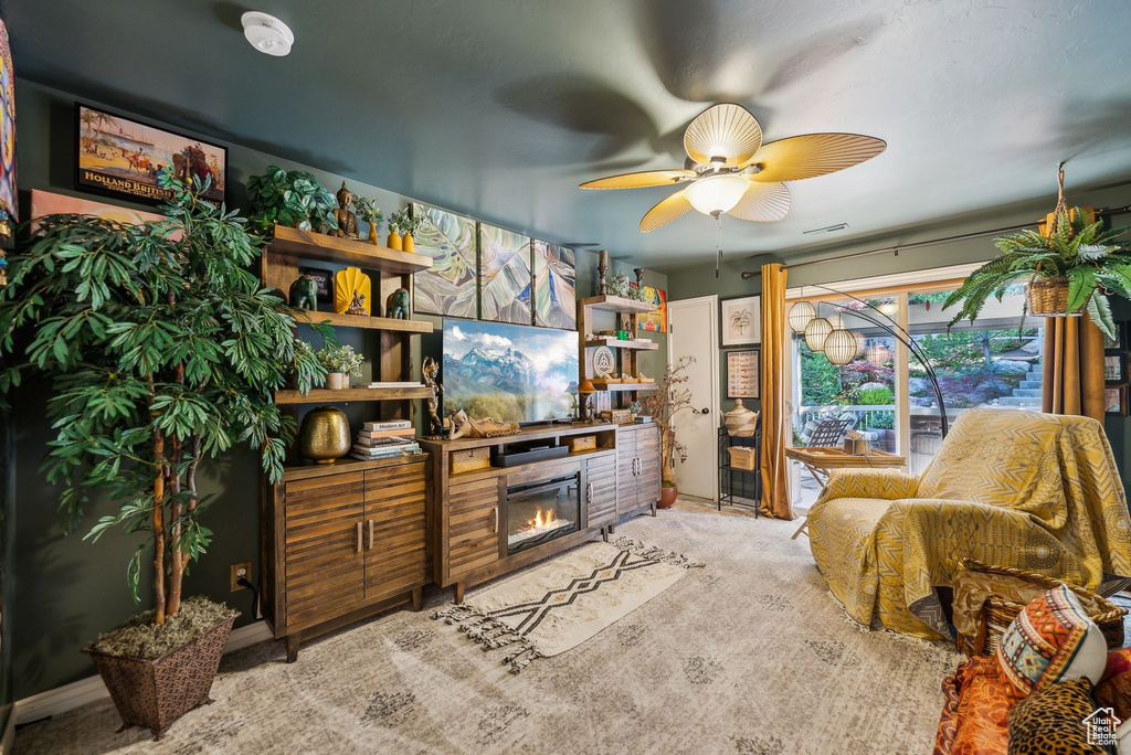 Living room with a glass covered fireplace, ceiling fan, and light colored carpet