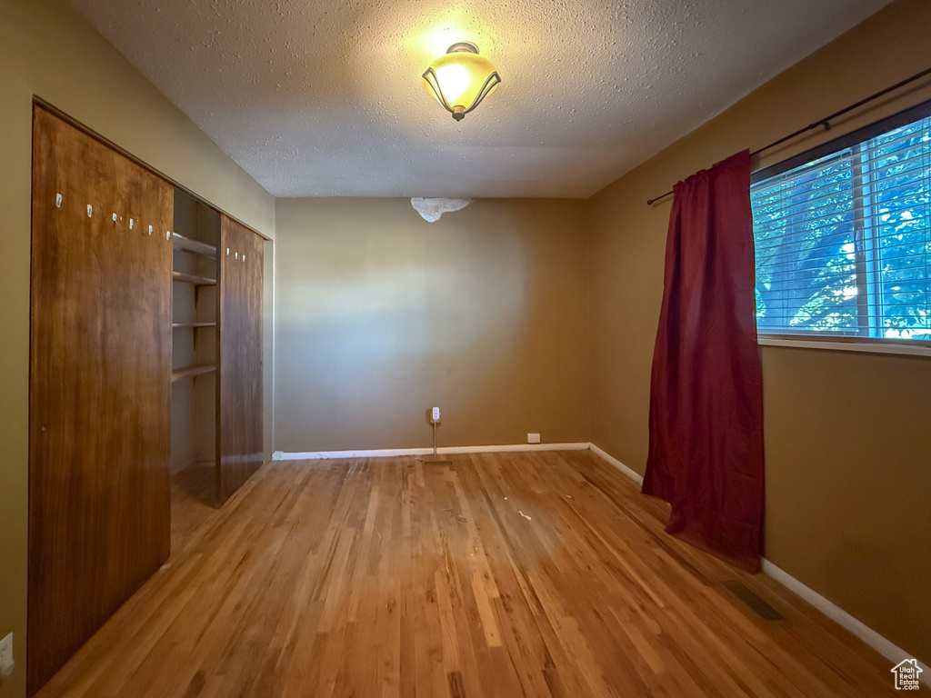 Unfurnished bedroom with wood finished floors, baseboards, a textured ceiling, and a closet