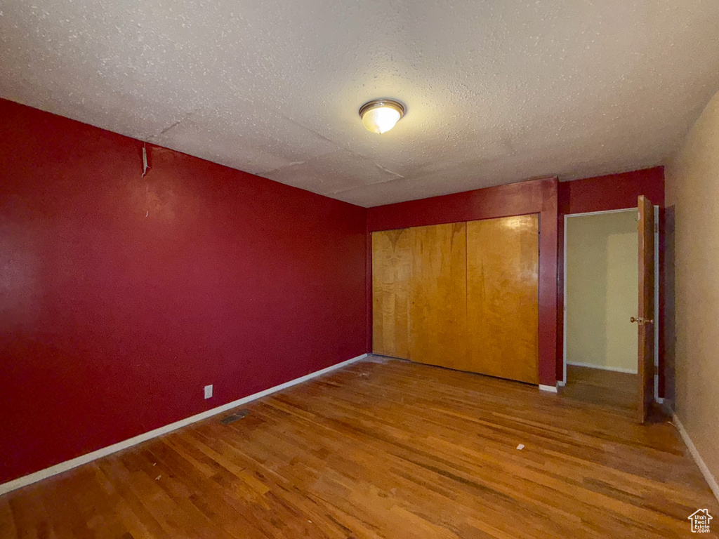 Unfurnished bedroom with wood finished floors, baseboards, a closet, and a textured ceiling