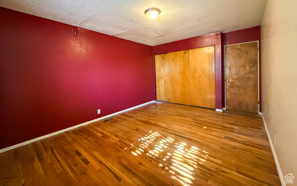 Unfurnished bedroom with wood finished floors, a textured ceiling, and baseboards
