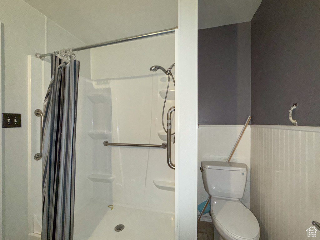 Bathroom featuring a shower with shower curtain, toilet, and a wainscoted wall