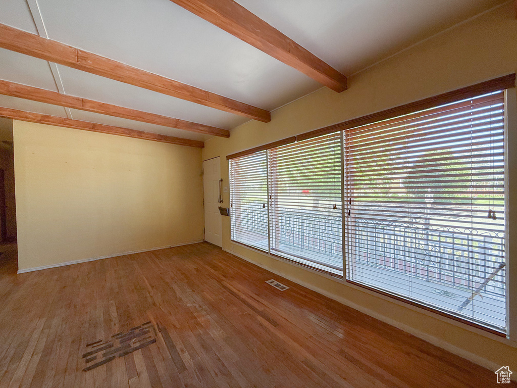Empty room with beamed ceiling, wood finished floors, and baseboards