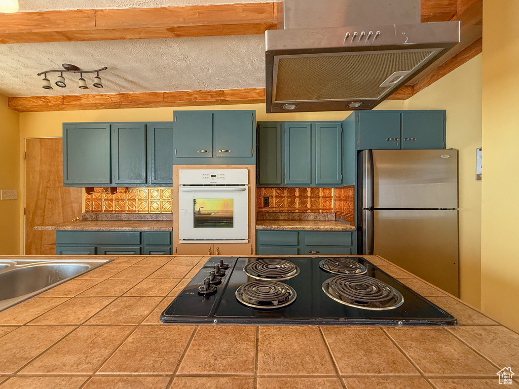 Kitchen featuring oven, black electric stovetop, freestanding refrigerator, and decorative backsplash