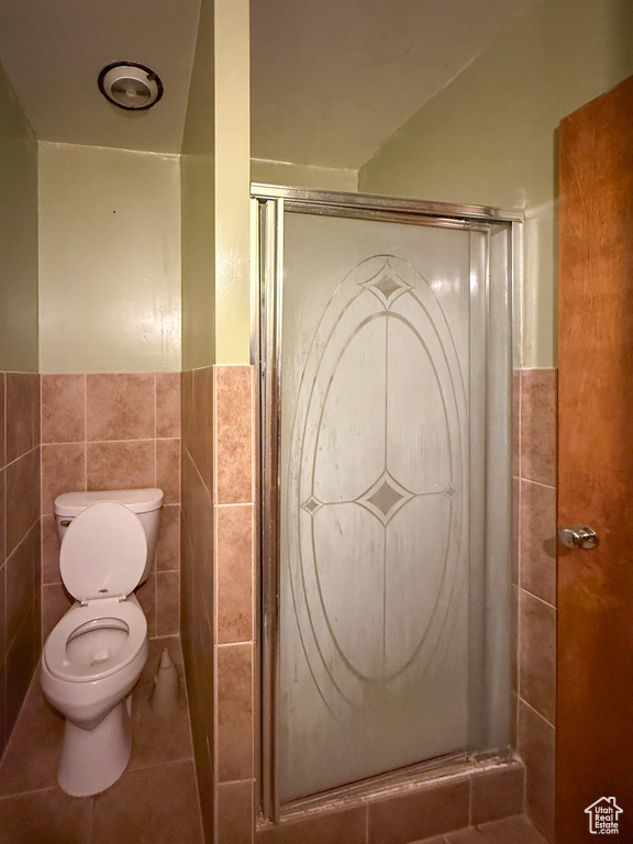 Bathroom with tile walls, toilet, a stall shower, a wainscoted wall, and tile patterned floors