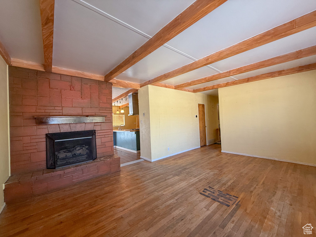 Unfurnished living room with beam ceiling, wood finished floors, baseboards, a stone fireplace, and a sink