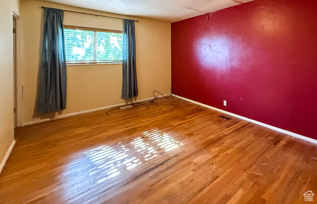 Empty room featuring wood finished floors, a textured ceiling, and baseboards
