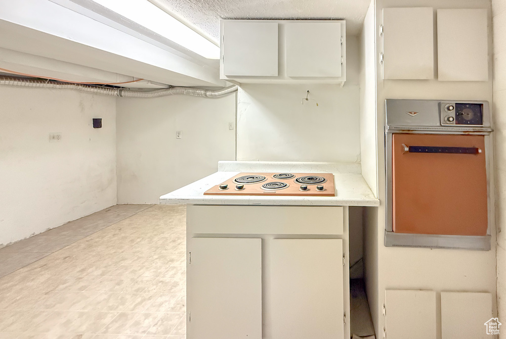 Kitchen featuring white electric cooktop, light countertops, white cabinets, and oven