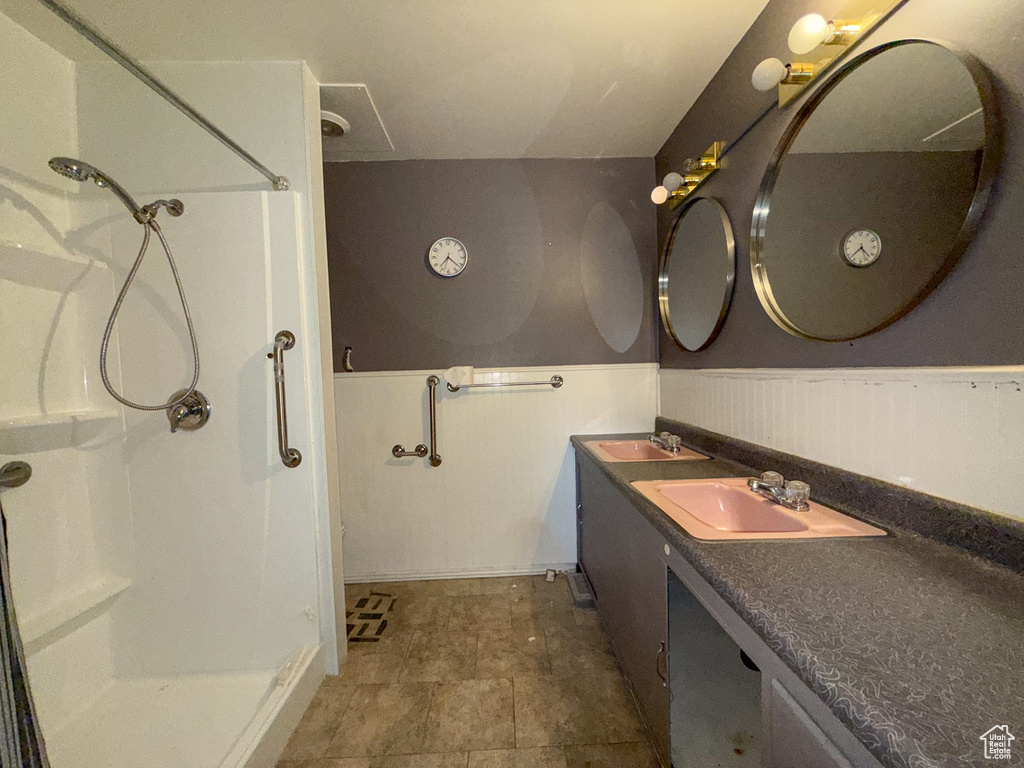 Full bath featuring walk in shower, double vanity, and wainscoting