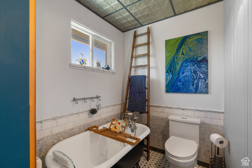 Bathroom featuring tile walls, a freestanding bath, wainscoting, an ornate ceiling, and toilet
