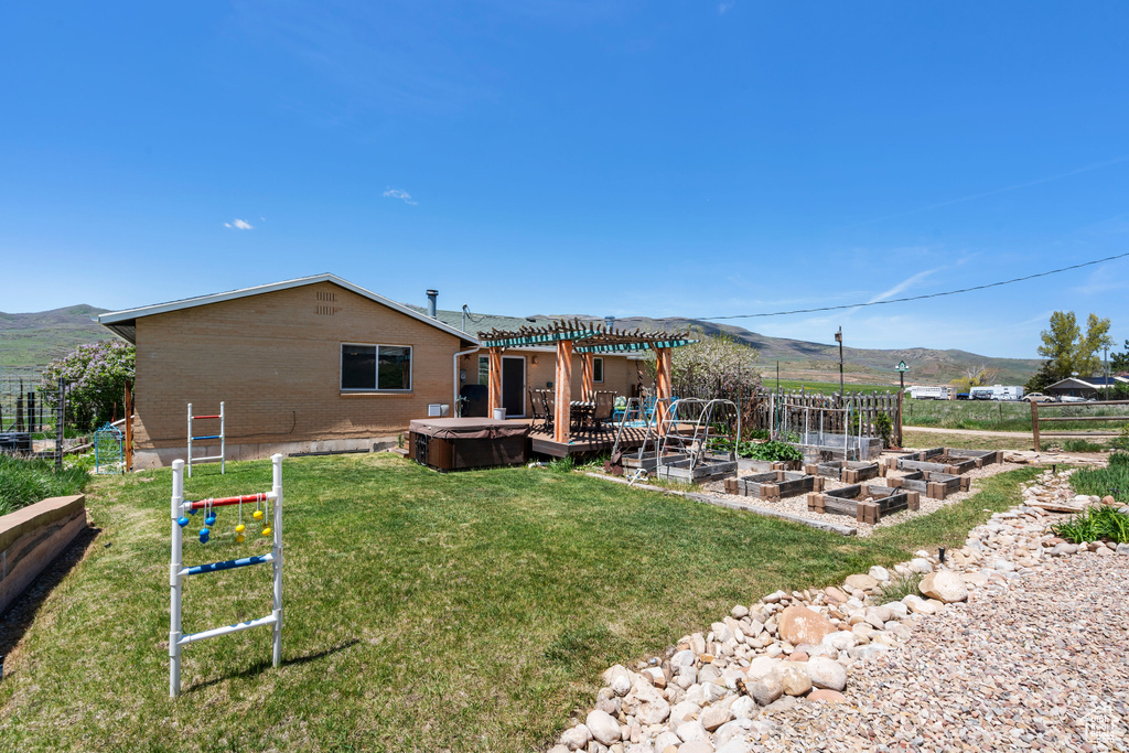 View of yard with a hot tub, a mountain view, a pergola, and a vegetable garden