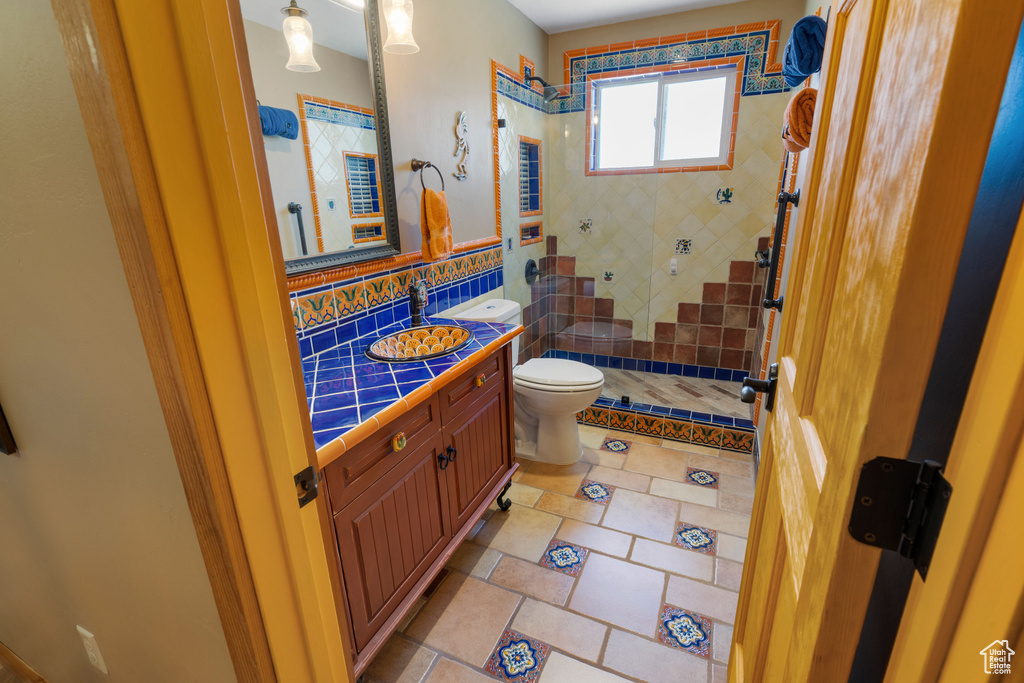 Full bath with toilet, tiled shower, and vanity