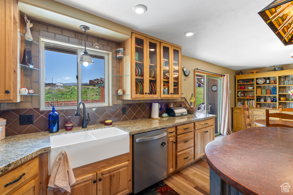 Kitchen with stainless steel dishwasher, a sink, light wood-style floors, and tasteful backsplash