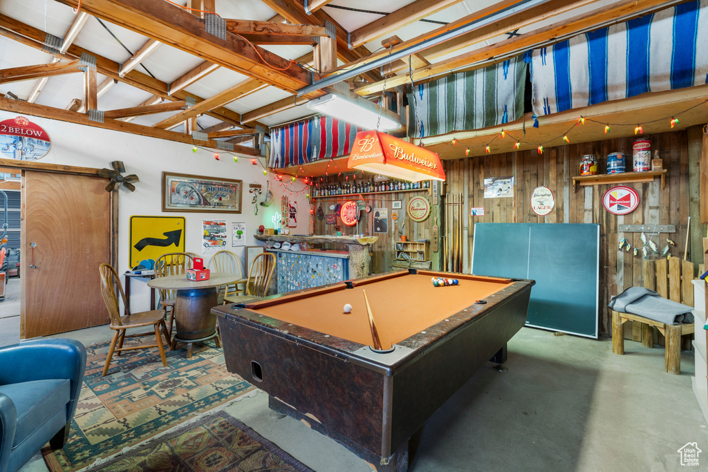 Playroom with pool table, wooden walls, concrete flooring, high vaulted ceiling, and bar area
