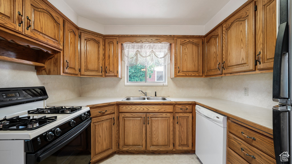 Kitchen featuring range with gas stovetop, white dishwasher, brown cabinets, and a sink
