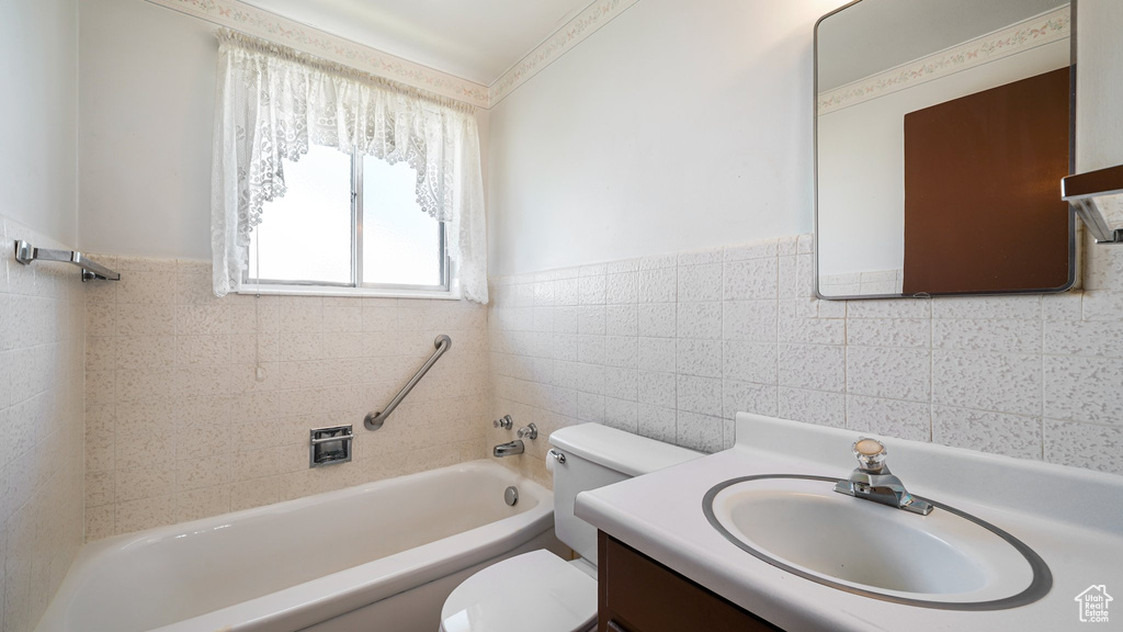 Bathroom with toilet, tile walls, vanity, wainscoting, and bathing tub / shower combination