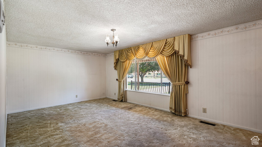 Carpeted empty room featuring a chandelier, a textured ceiling, and baseboards