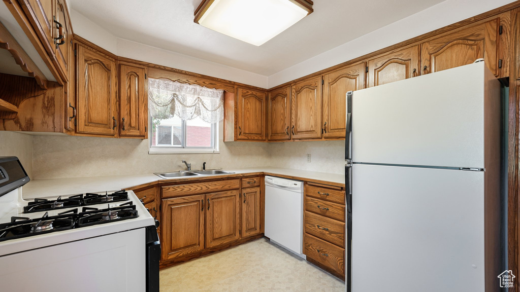 Kitchen with white appliances, brown cabinetry, a sink, light countertops, and light flooring