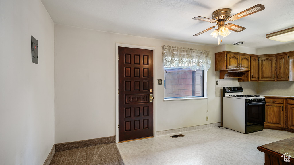 Kitchen with range with gas cooktop, a ceiling fan, brown cabinets, and baseboards
