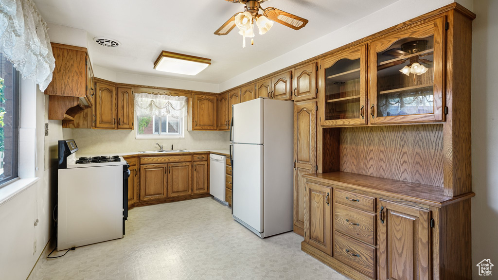 Kitchen featuring white appliances, brown cabinetry, ceiling fan, light floors, and glass insert cabinets