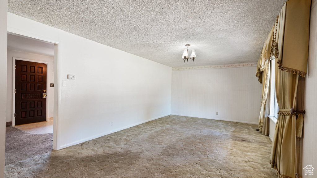 Spare room with a chandelier, light carpet, baseboards, and a textured ceiling