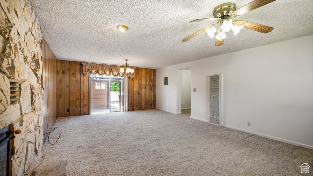 Unfurnished living room featuring a heating unit, a textured ceiling, wood walls, carpet, and a ceiling fan