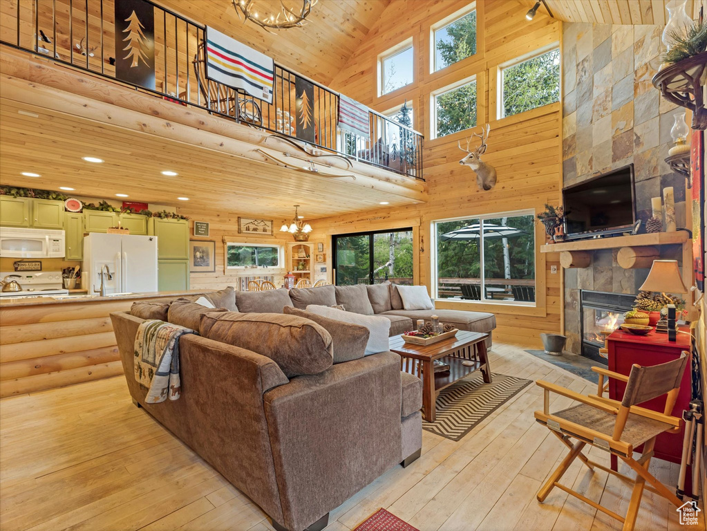 Living room featuring high vaulted ceiling, a stone fireplace, light wood-type flooring, a chandelier, and wood ceiling