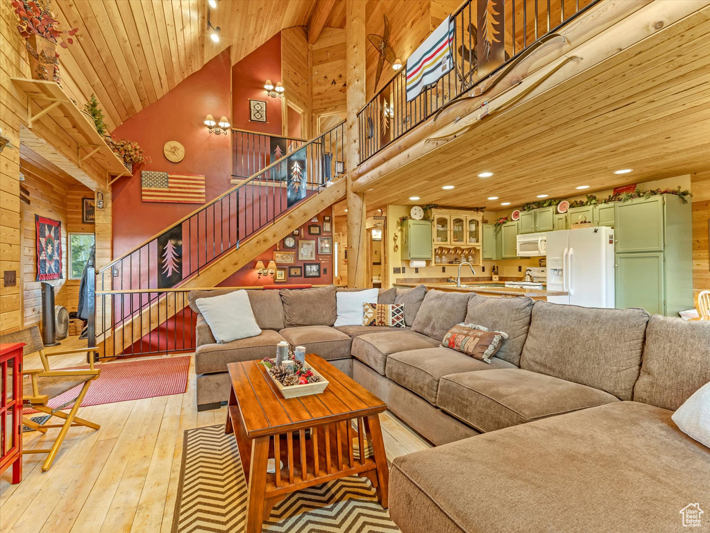 Living room with high vaulted ceiling, wood ceiling, light wood-style flooring, stairs, and wooden walls