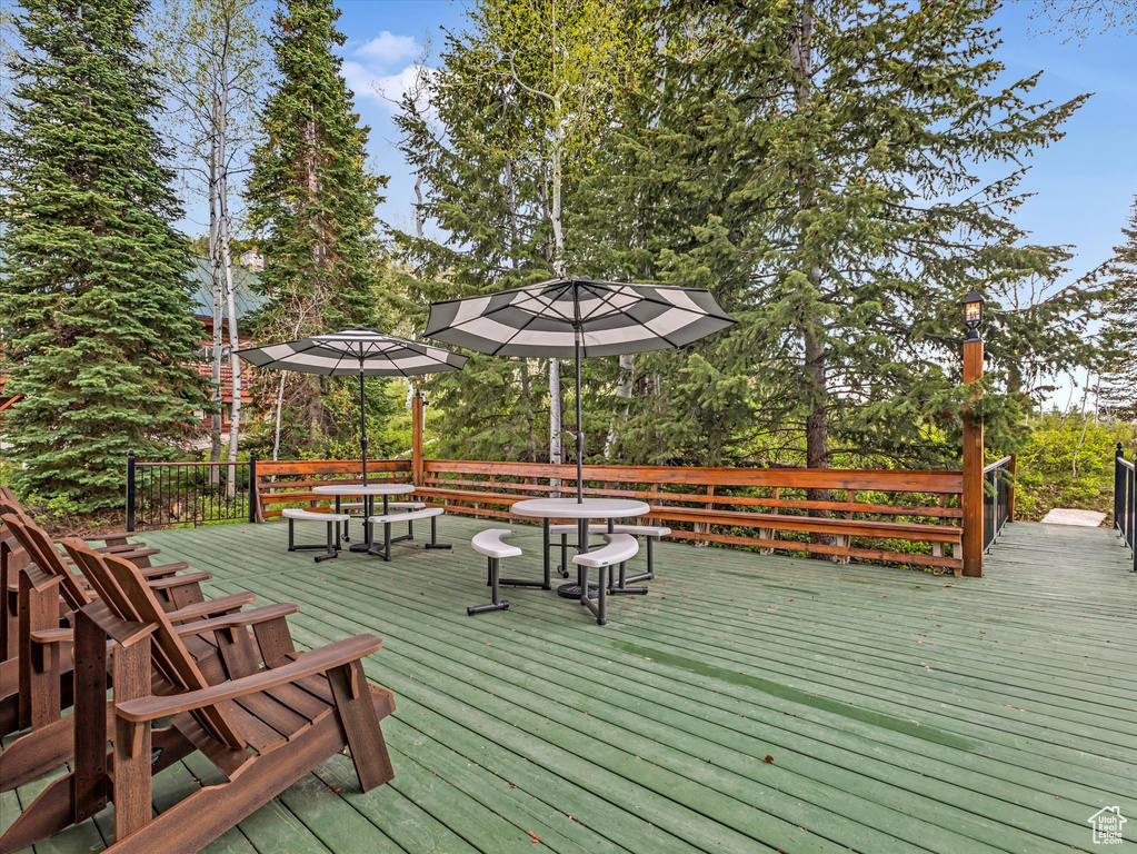 Wooden terrace featuring outdoor dining area and view of wooded area