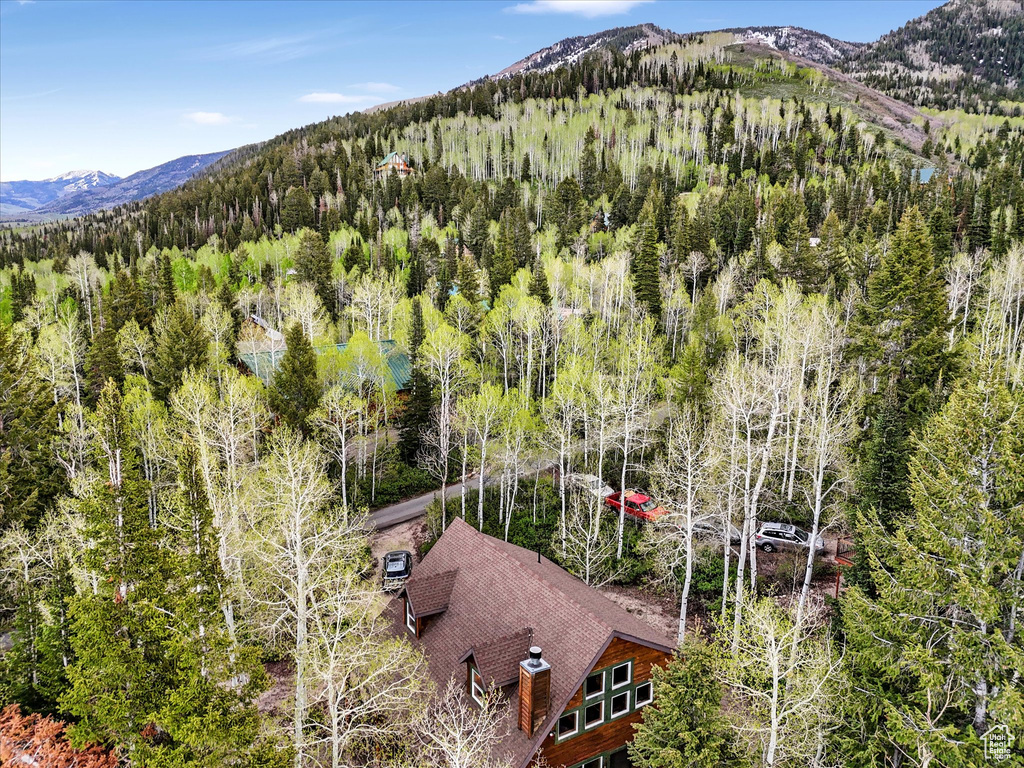 Aerial view of property and surrounding area featuring a mountainous background and a forest