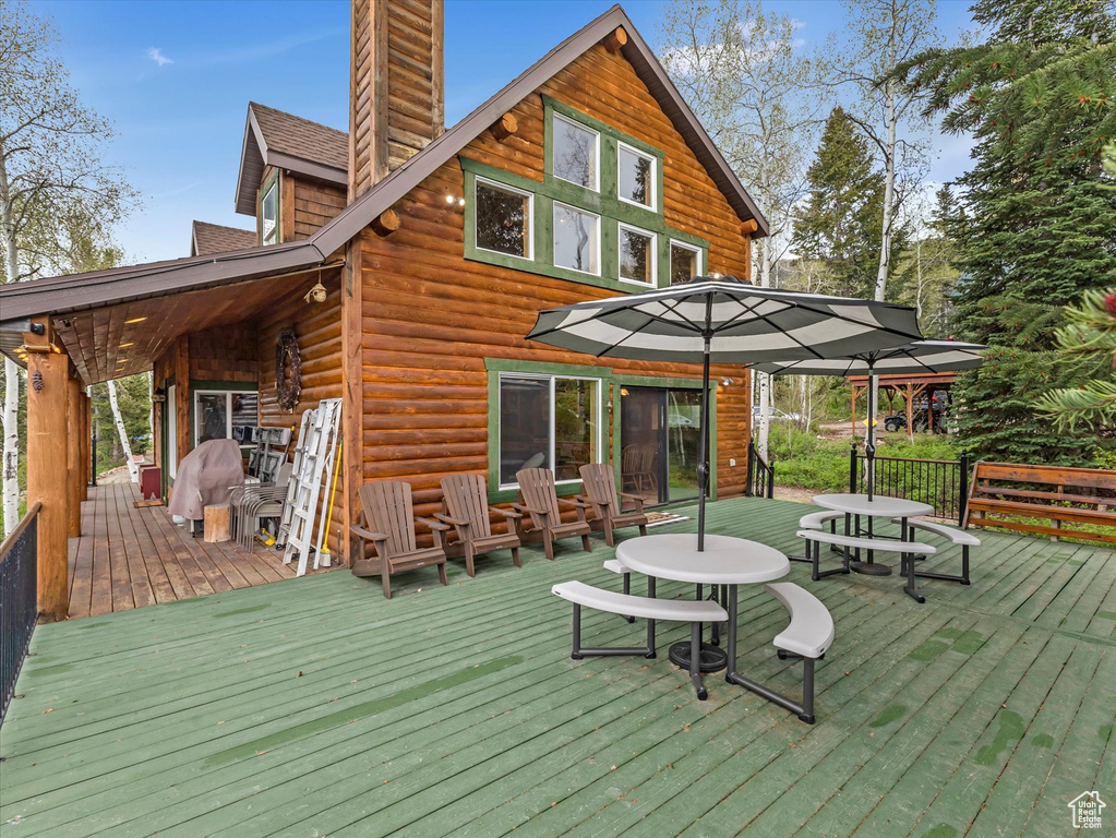 Rear view of house with a chimney, a wooden deck, and outdoor dining space