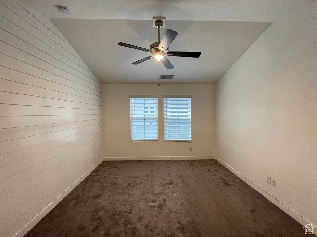 Spare room with a smoke detector, baseboards, wood walls, vaulted ceiling, and a ceiling fan