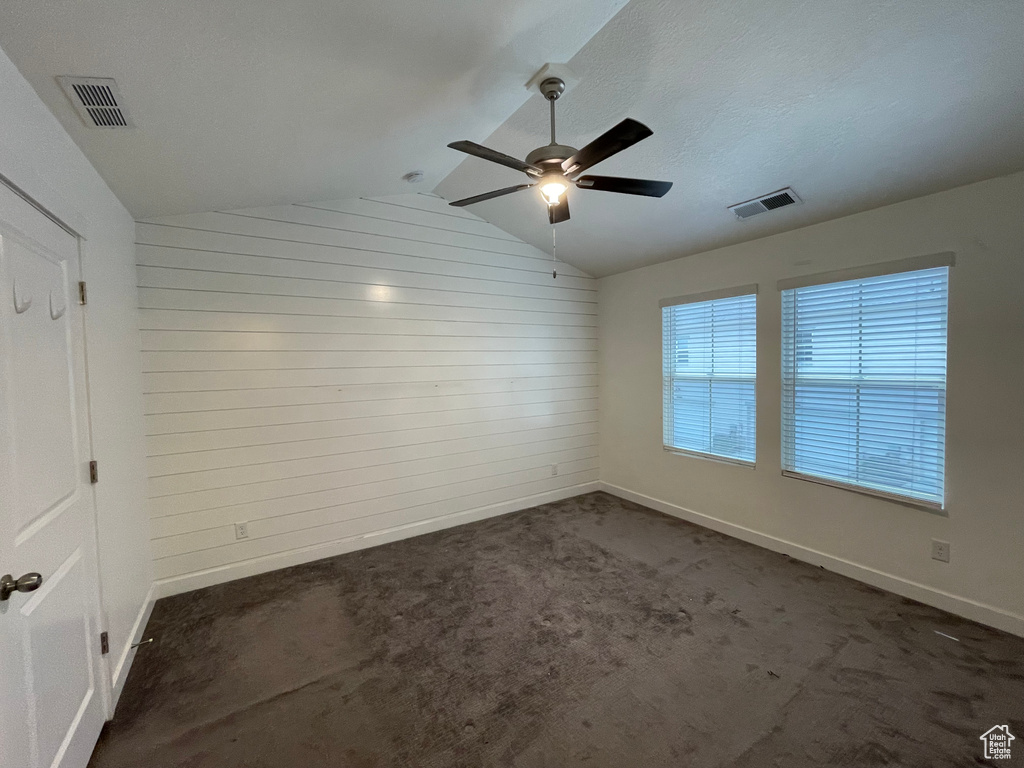 Spare room featuring lofted ceiling, wooden walls, baseboards, ceiling fan, and dark carpet