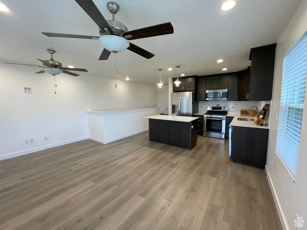 Kitchen with appliances with stainless steel finishes, a sink, a kitchen island, light countertops, and open floor plan