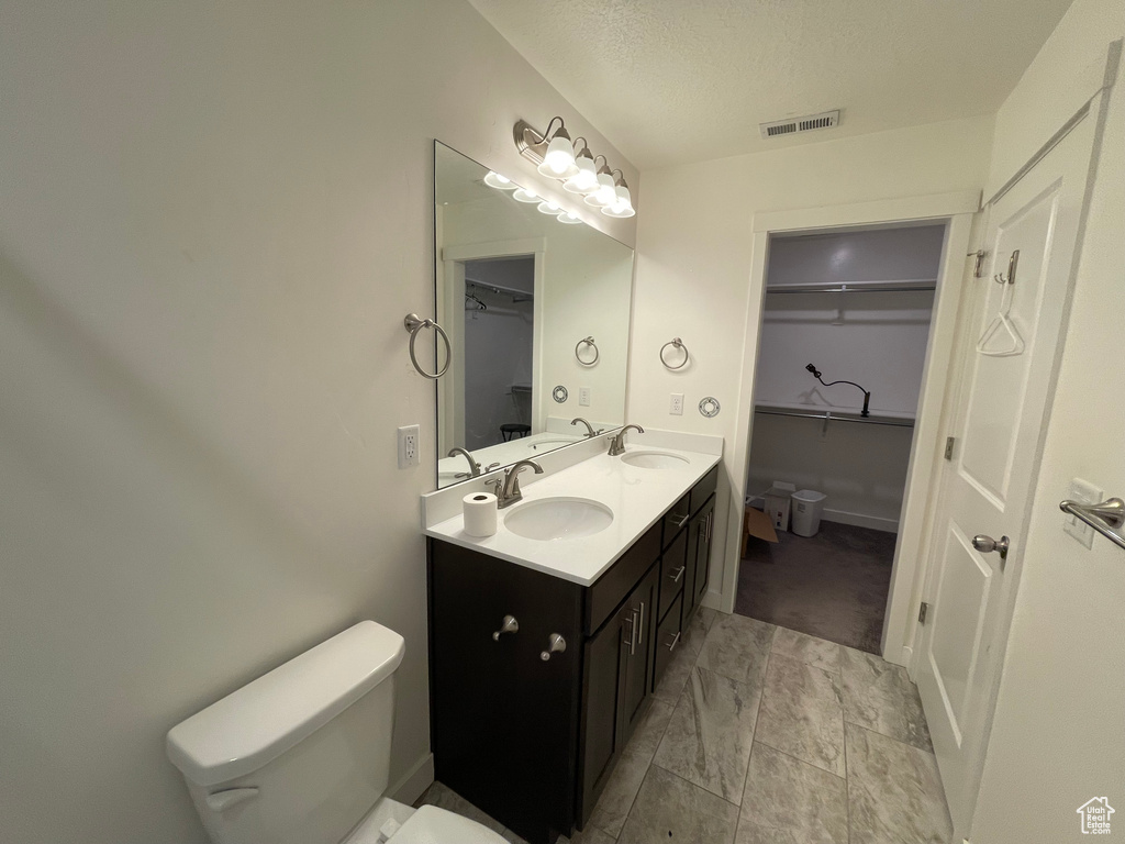 Full bathroom with toilet, double vanity, a walk in closet, a textured ceiling, and marble look tiles