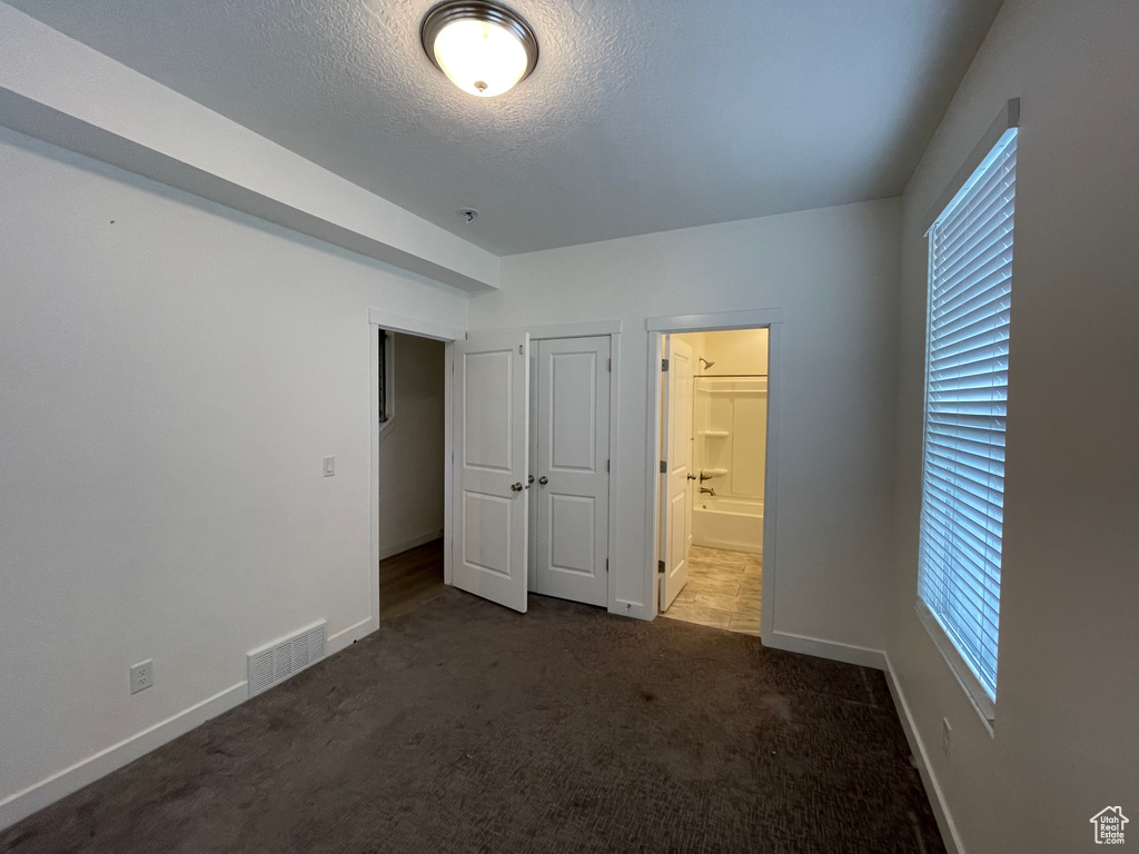 Unfurnished bedroom featuring carpet flooring, baseboards, a textured ceiling, ensuite bath, and a closet