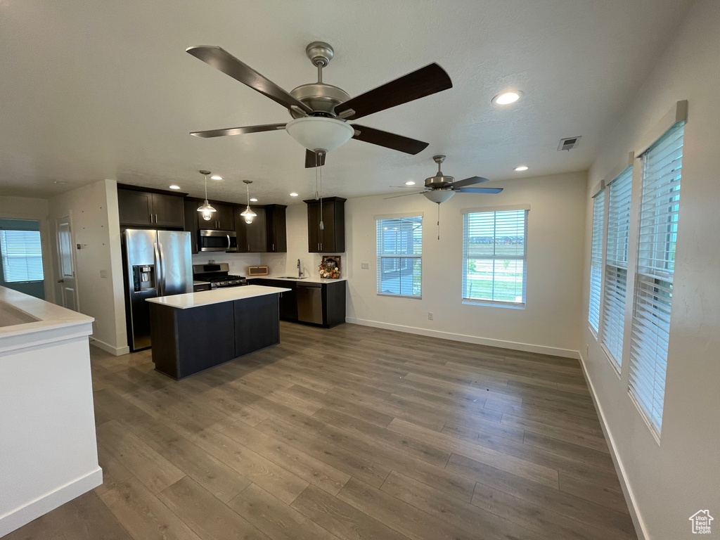 Kitchen with appliances with stainless steel finishes, a center island, a sink, light countertops, and baseboards