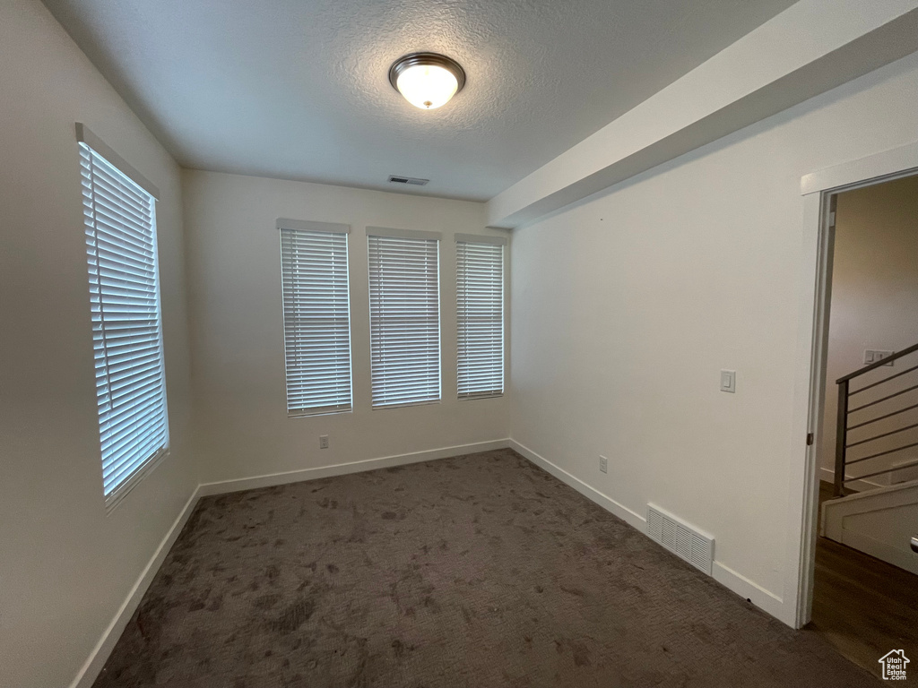 Carpeted empty room with baseboards, a textured ceiling, and stairway