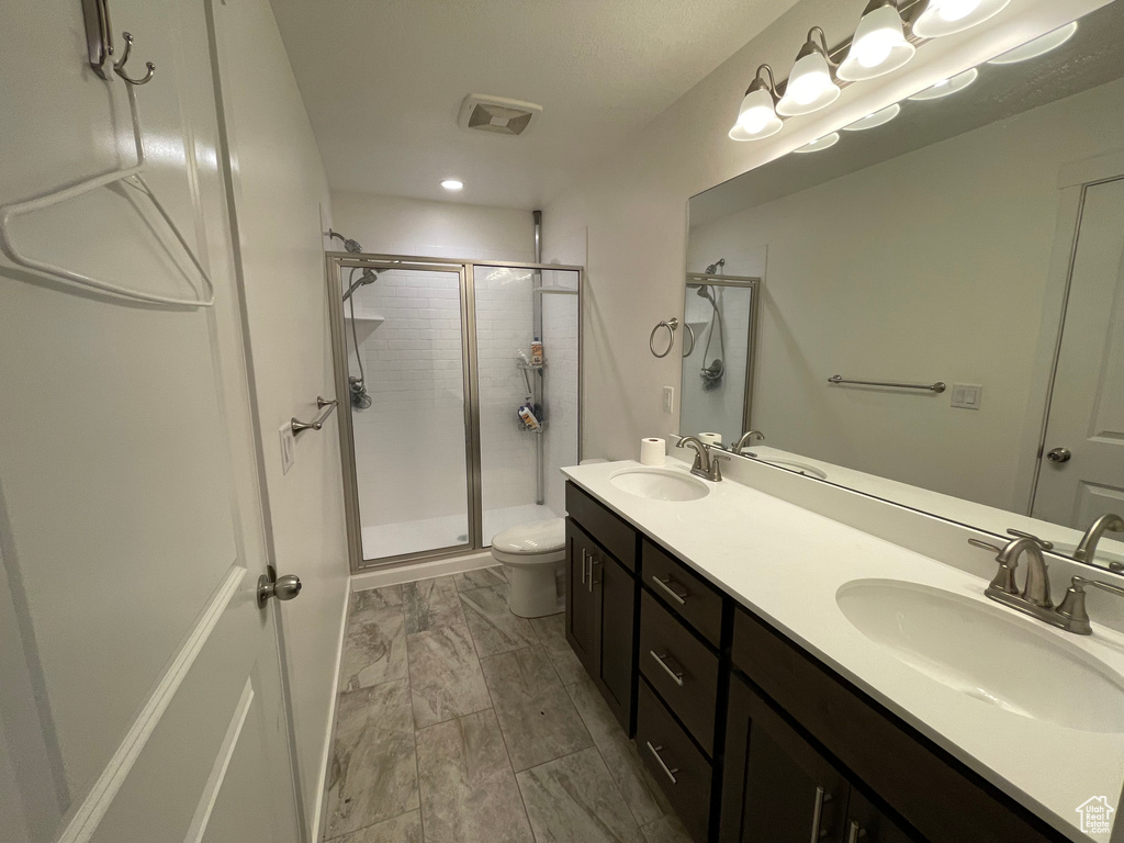 Bathroom featuring a stall shower, double vanity, toilet, and marble finish floors