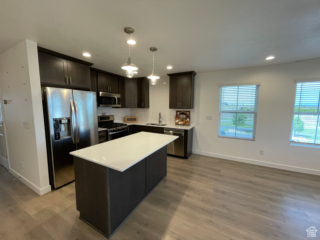 Kitchen with appliances with stainless steel finishes, a sink, light wood-style flooring, baseboards, and light countertops