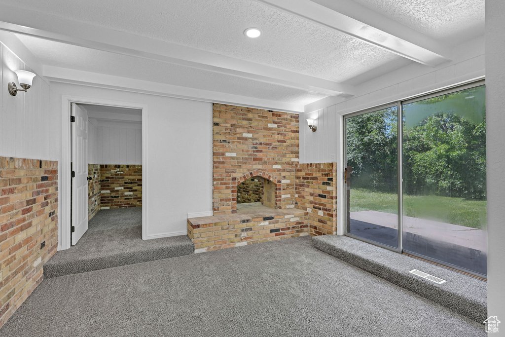 Unfurnished living room featuring carpet flooring, beam ceiling, brick wall, a textured ceiling, and a brick fireplace