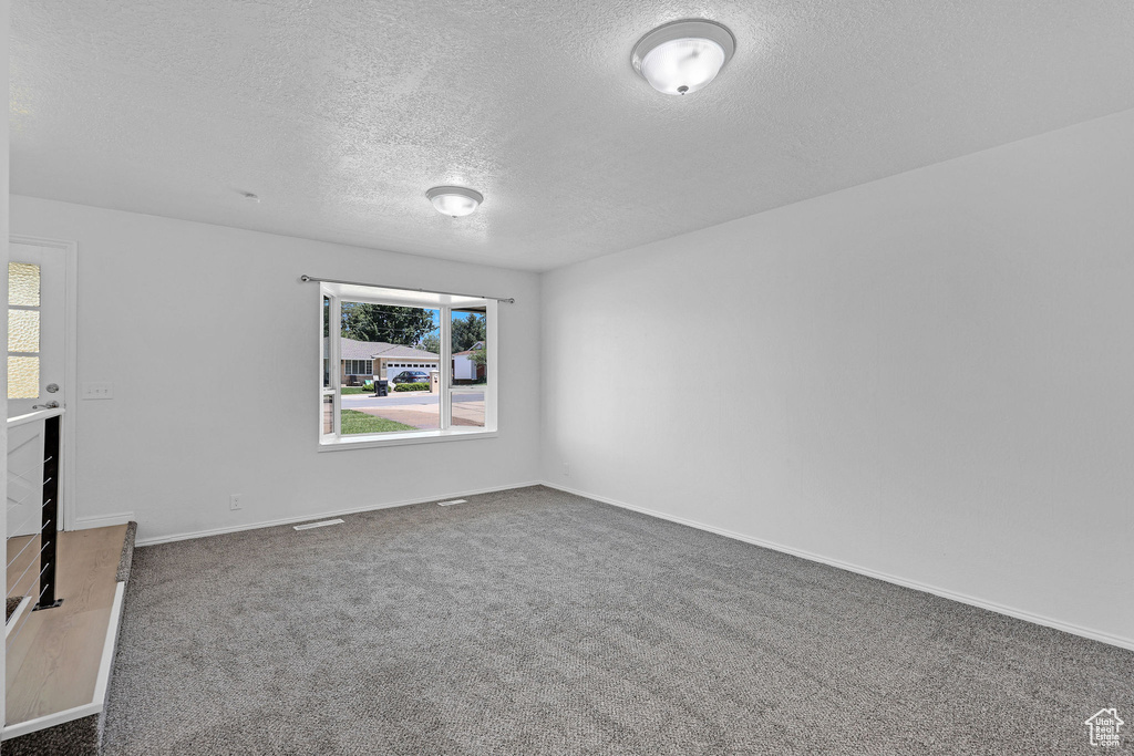 Carpeted spare room featuring a textured ceiling and baseboards